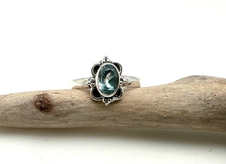 May include: A silver ring with a light blue oval gemstone set in a floral design.