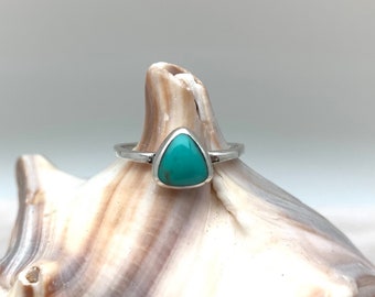 May include: A silver ring with a triangular turquoise gemstone. The ring is displayed on a seashell.