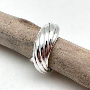 May include: A silver ring with a unique, twisted design. The ring is made of smooth, polished metal and has a wide band.