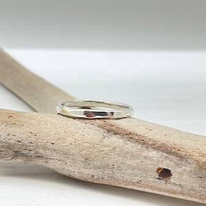 Pode incluir: Um anel de banda de prata martelada, descansando sobre um pedaço de madeira à deriva.