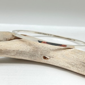 May include: A simple silver bangle bracelet with a flat, polished finish.