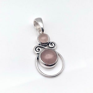 Peut inclure: Un pendentif en argent avec deux pierres de quartz rose. Le pendentif pr&eacute;sente un design d&eacute;licat et tourbillonnant.