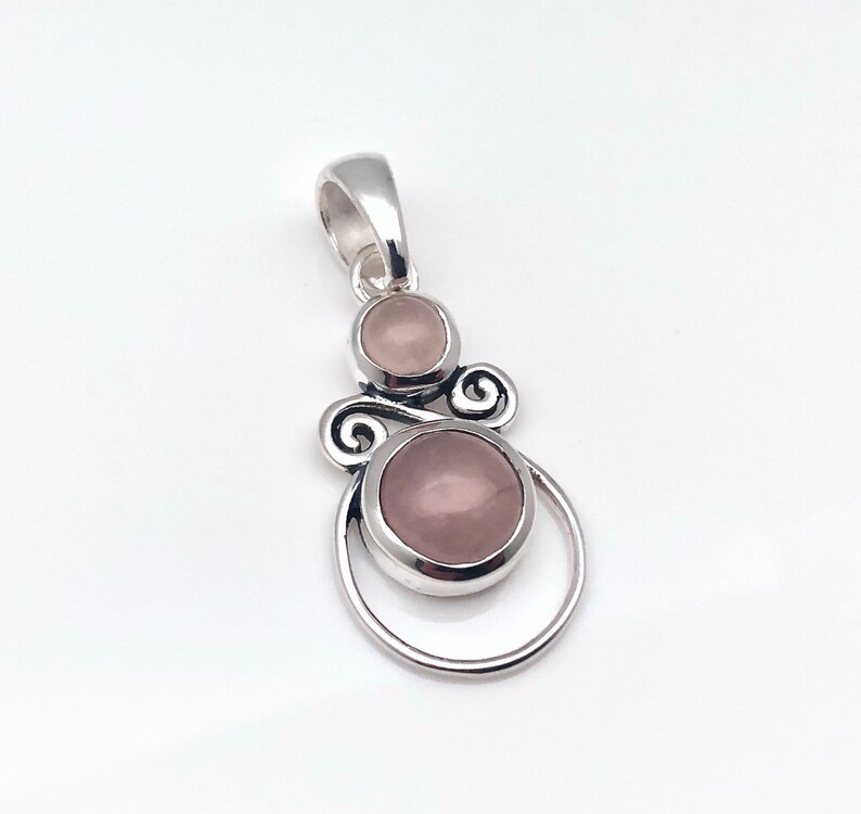 Peut inclure: Un pendentif en argent avec deux pierres de quartz rose. Le pendentif pr&eacute;sente un design d&eacute;licat et tourbillonnant.