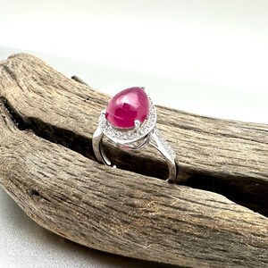 May include: A silver ring with a pear-shaped ruby gemstone surrounded by a halo of smaller diamonds.