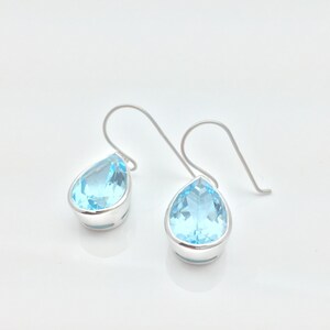 May include: A pair of silver teardrop earrings with light blue topaz stones.