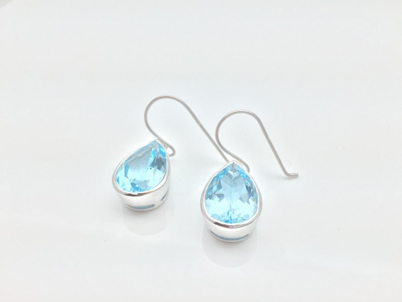 May include: A pair of silver teardrop earrings with light blue topaz stones.