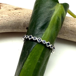 May include: A silver band ring with a row of dark blue square-shaped gemstones set in a geometric pattern.