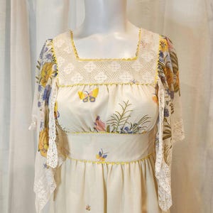 May include: A vintage cream-colored dress with a square neckline and butterfly and floral print. The dress features a yellow trim, lace detailing, and sheer sleeves. The dress is displayed on a mannequin.