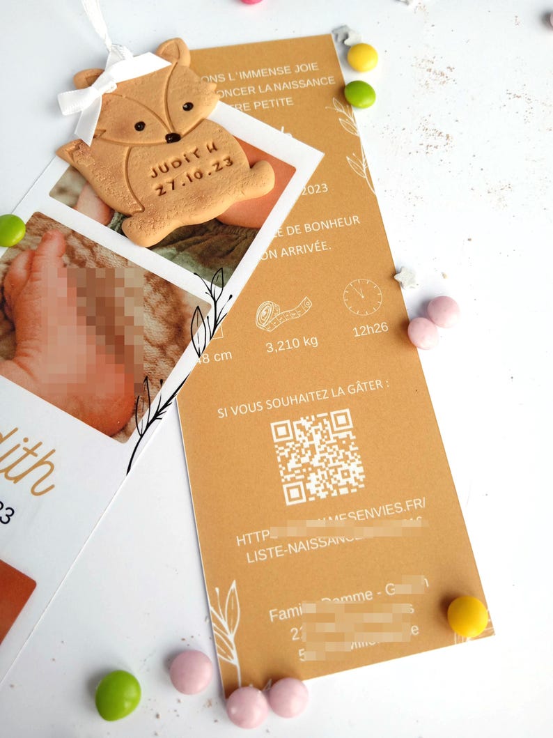 May include: A baby announcement card with a fox-shaped cookie and a photo. The card is tan with text in French, including the baby's name, Judith, and birthdate, 27.10.23. The card also includes the baby's weight, 3.210 kg, and length, 8 cm.