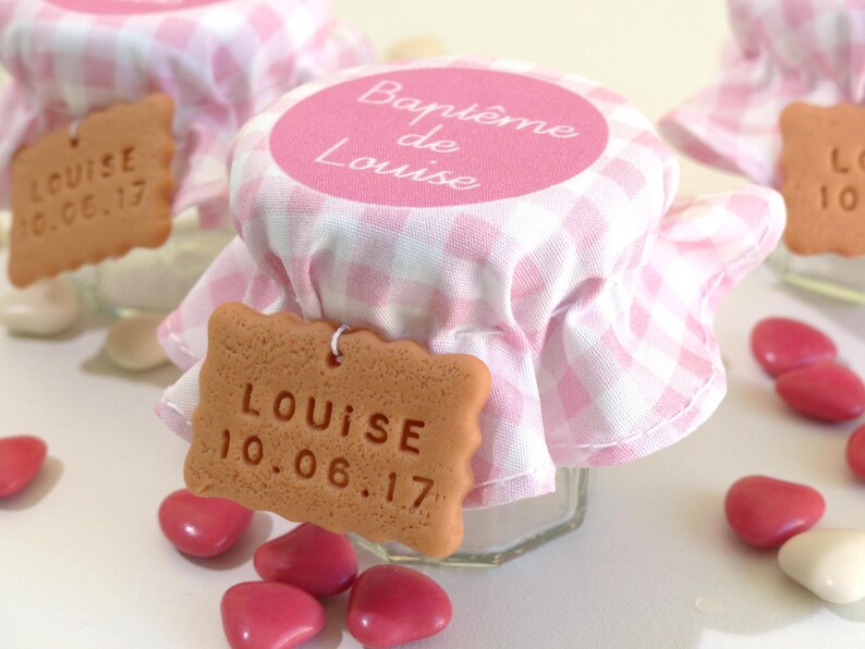 May include: Pink and white checkered fabric jar with a brown cookie-shaped tag that says "LOUISE 10.06.17". The jar has a pink circle label that says "Bapt&ecirc;me de Louise".