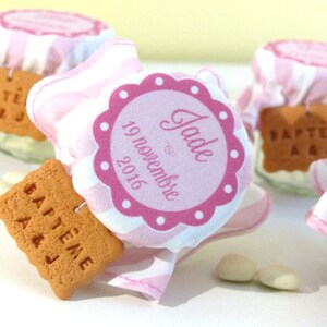 May include: Pink and white striped fabric jars with a pink circle label that says "Jade" and "19 novembre 2016". Each jar has a small, round, brown cookie with the text "BAPT&Ecirc;ME A&J" on it.