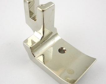 May include: A silver sewing machine foot with a curved edge and a small hole in the center.