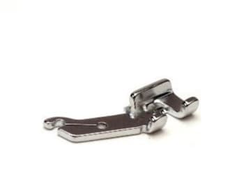 May include: A silver sewing machine foot with a curved metal arm and a small hole in the center.