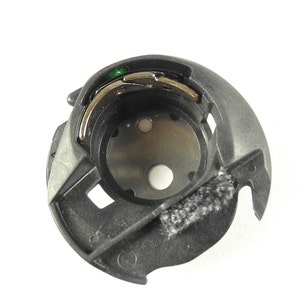 Op de afbeelding: Een zwarte plastic spoelhouder met een zilveren metalen spoel en een groene plastic draadgeleider.