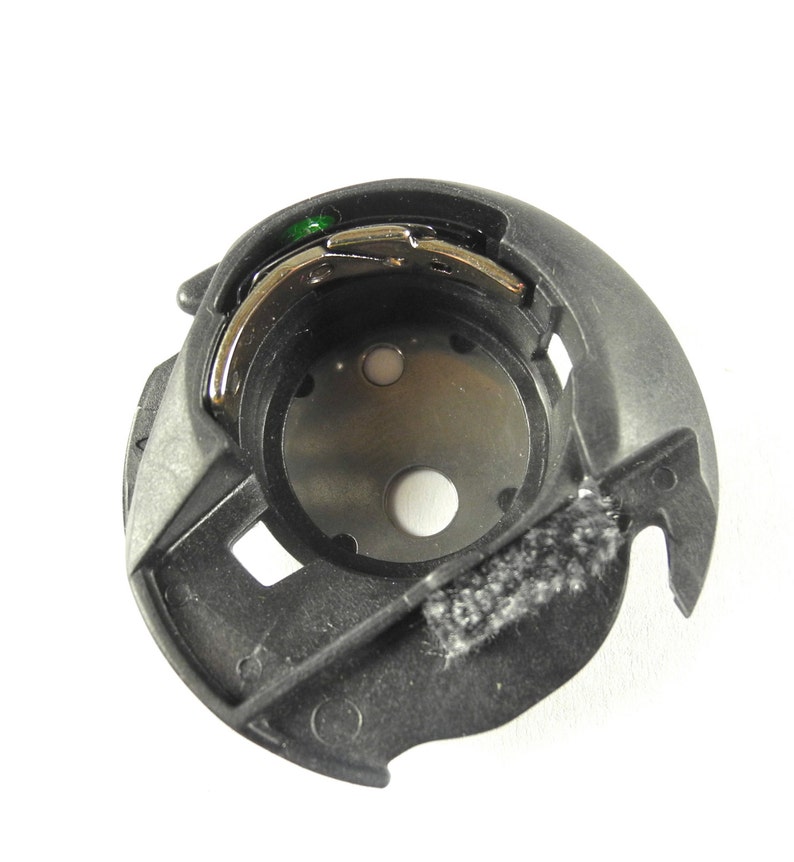 Op de afbeelding: Een zwarte plastic spoelhouder met een zilveren metalen spoel en een groene plastic draadgeleider.