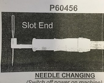 May include: Diagram of a needle changing tool with the text "Slot End" and "Needle Changing (Switch off power on machine)". The tool is white and has a needle attached to it. The background is a dark gray.