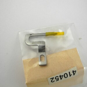 May include: A silver sewing machine foot with a yellow plastic needle guide. The foot is labeled with the number 410452.