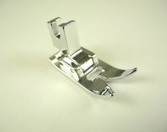 May include: A silver sewing machine foot with a raised metal piece on the top.