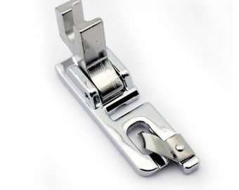 May include: A silver sewing machine foot with a metal guide and a spring-loaded mechanism.