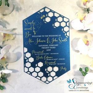 May include: A blue and gold wedding invitation with a honeycomb pattern. The invitation reads "Simply meant to Bee" and includes the names "Alice Johnson & John Smith". The invitation also includes the date "Saturday, February Twenty Third, 2018" and the names of the songs that will be played during the ceremony.