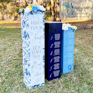 May include: Three tall, blue and white floral patterned wedding table number signs. The first sign says "Find Your Seat It's Time To Eat Alice & John". The second sign is dark blue and has the numbers 1 through 6 with names listed next to each number. The third sign is light blue and has the numbers 7 through 11 with names listed next to each number.