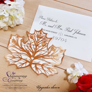 May include: A laser cut invitation in the shape of a copper-colored maple leaf with a white background. The invitation features the text "Shimmering Ceremony" and "Laser Cut Invitations". The text "Upgrades shown" is also visible at the bottom of the image.