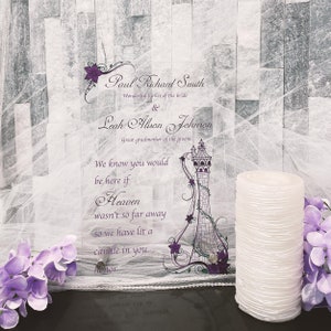 May include: A clear acrylic wedding memorial sign with purple floral accents and text. The sign reads "Paul Richard Smith, Wonderful father of the bride & Leah Alison Johnson, Great grandmother of the groom." A white pillar candle and purple flowers are also in the image.