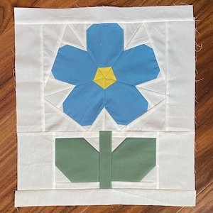 May include: A blue and yellow flower with a green stem, made from fabric squares, on a white background.