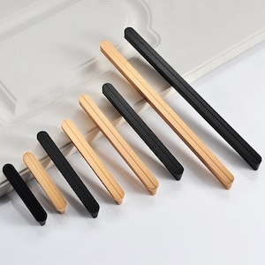 May include: A set of seven cabinet pulls in two finishes: black and gold. The pulls are rectangular with a flat, slightly rounded edge. The pulls are arranged in order of size, with the smallest pull on the left and the largest pull on the right.