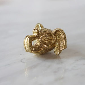 May include: A gold-coloured elephant charm with a detailed textured surface. The elephant's trunk is curled up, and its ears are large and floppy.
