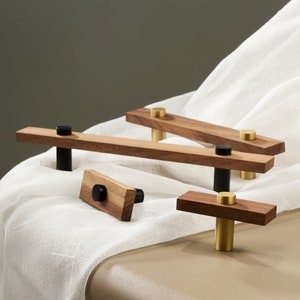 May include: Four wooden cabinet knobs with black and gold accents. The knobs are made of dark wood and have a rectangular shape. The knobs are arranged on a white surface.