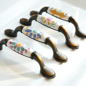 May include: Four antique bronze cabinet knobs with white ceramic fronts featuring colourful floral designs.
