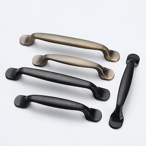 Peut inclure: Quatre poignées de porte en deux finitions : laiton antique et noir. Les poignées sont toutes du même style, avec une forme rectangulaire arrondie et une légère courbe.