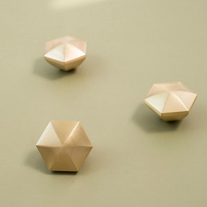 Op de afbeelding: Drie gouden, geometrische draaitopjes met een stervormig ontwerp. De draaitopjes zijn gemaakt van metaal en hebben een geborstelde afwerking.