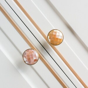 May include: Two round cabinet knobs with a gold metal base and a shell inlay. The shell inlay is a light pink and peach colour with a geometric pattern.