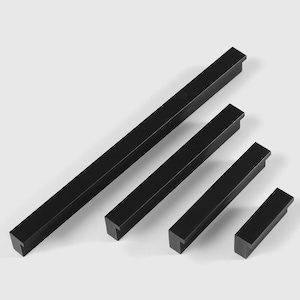 以下が含まれることがあります： 異なるサイズの黒い金属製のキャビネットプルが4つ。プルは長方形で、端がT字型にカットされています。