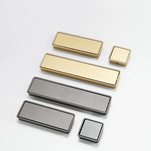 May include: Assortment of cabinet hardware pulls in gold and grey finishes. The pulls are rectangular and square in shape.