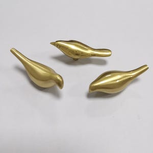May include: Three gold-coloured metal bird figurines. The birds are in a variety of poses, with one facing forward, one facing to the left, and one facing to the right.