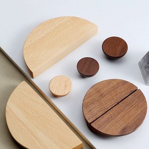 May include: Set of wooden cabinet knobs and pulls in two different wood tones. The knobs are round and the pulls are half-circle shapes.