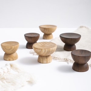 Può includere: Cinque pomelli in legno di diverse dimensioni e tonalità di marrone. I pomelli hanno una parte superiore arrotondata e una base a piedistallo.