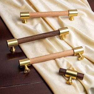 Peut inclure: Trois poignées de tiroir avec une poignée en bois et des accents en métal doré. Les poignées sont de différentes longueurs et de différents types de bois.