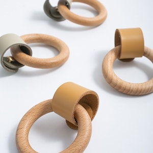 以下が含まれることがあります： 革のストラップが付いた木製のリングプルが4つ。2つのプルには薄い茶色の革のストラップが付いており、2つのプルには薄い緑色の革のストラップが付いています。