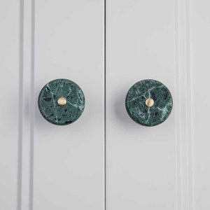 Könnte beinhalten: Zwei runde grüne Marmorknopf für Schränke mit einem goldenen Metallakzent in der Mitte.
