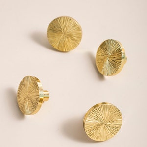 Puede incluir: Cuatro pomos redondos de armario de color dorado con un diseño de sol.