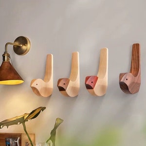 May include: Four wooden bird-shaped wall hooks in different shades of brown. The hooks are mounted on a white wall.