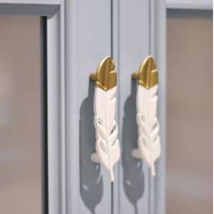 以下が含まれることがあります： 金色のアクセントが付いた白い羽根の形をしたキャビネットノブが2つ。ノブは薄い青色のキャビネットドアに取り付けられています。