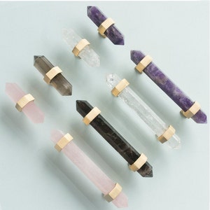 May include: Assortment of eight crystal cabinet knobs in various colours, including amethyst, clear quartz, rose quartz, and smoky quartz. Each knob features a gold-toned metal base.