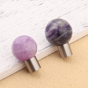 Könnte beinhalten: Zwei Kristallkugel-Schrankknöpfe in Lila und Lavendel mit silbernen Metallsockeln.