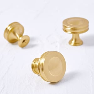 Peut inclure: Trois boutons de porte en or avec un centre rond légèrement surélevé et une finition lisse et polie. Les boutons ont un design simple et élégant.