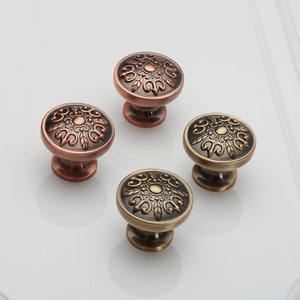 May include: Four ornate cabinet knobs with a floral design. Two knobs are copper and two are bronze.